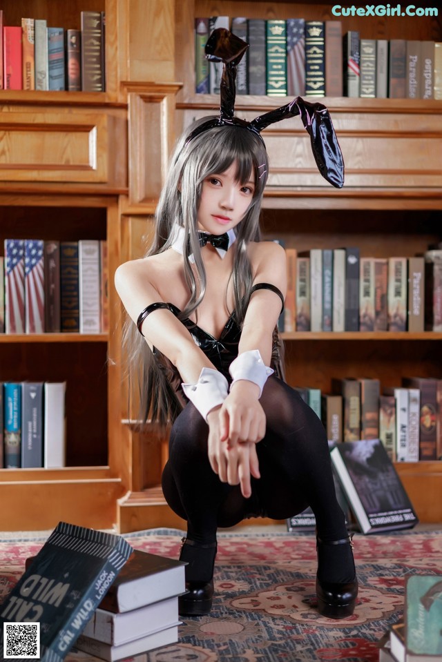 A woman sitting on the floor in front of a bookshelf.