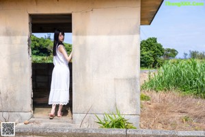 A woman in a white dress leaning against a wall.