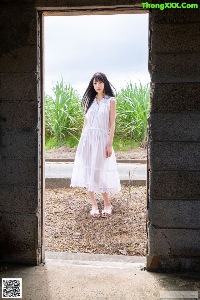 A woman in a white dress standing in an open doorway.