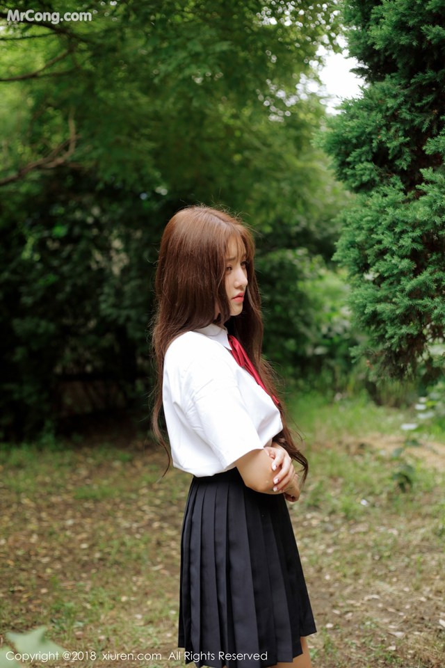 A woman in a school uniform standing in the woods.