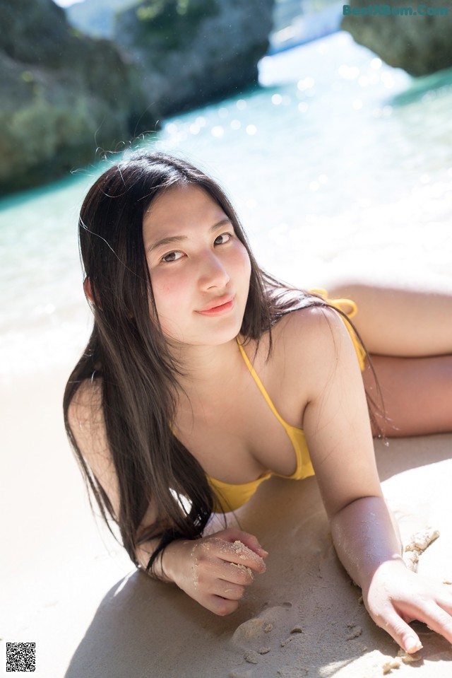 A woman in a yellow bikini laying on the beach.