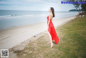 A woman in a red dress leaning against a palm tree.