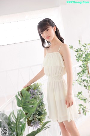 A woman sitting on a bed in a white dress.