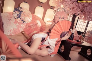 A woman with pink hair sitting on a bed.
