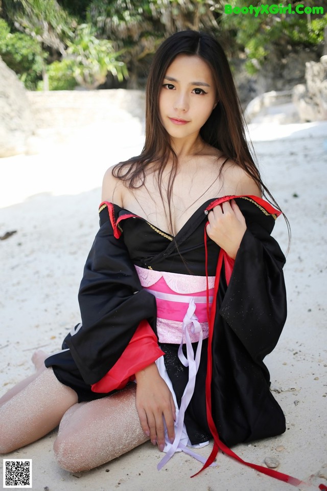 A woman in a black and red kimono sitting on a beach.