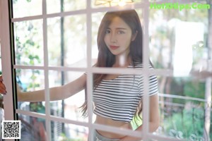 A woman in a white shirt and denim shorts posing by a window.