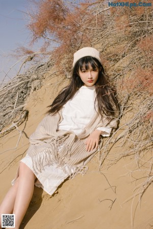 A woman standing in the sand wearing a white hat and scarf.