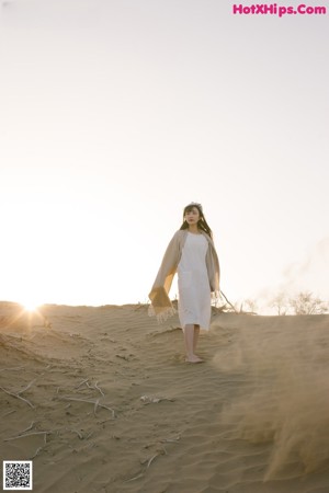 A woman in a white dress and hat standing on a sand dune.