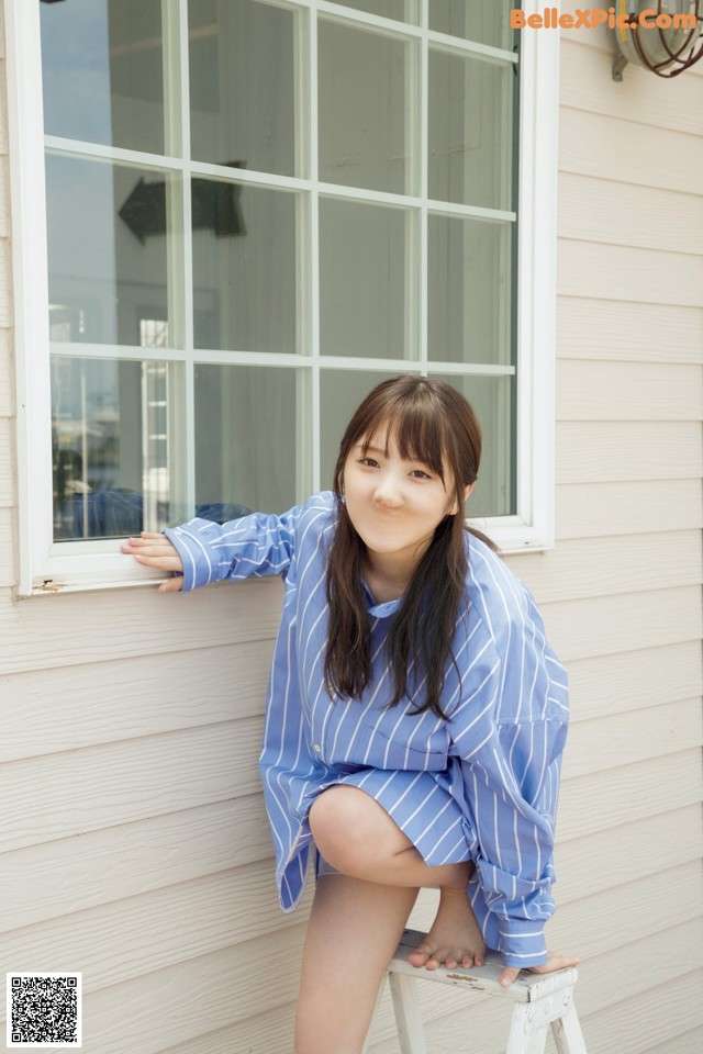 A woman sitting on a stool in front of a window.