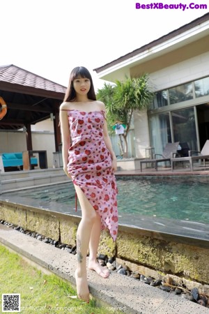 A woman in a pink dress leaning against a wall.