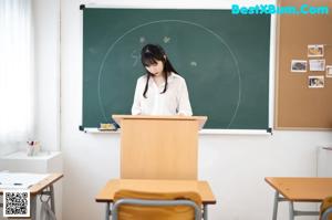 A woman in a white shirt and black skirt leaning on a desk.