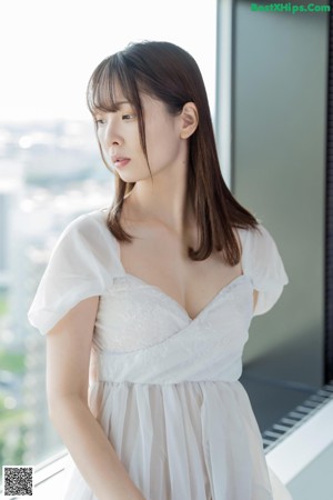 A woman in a white dress sitting on a window sill.