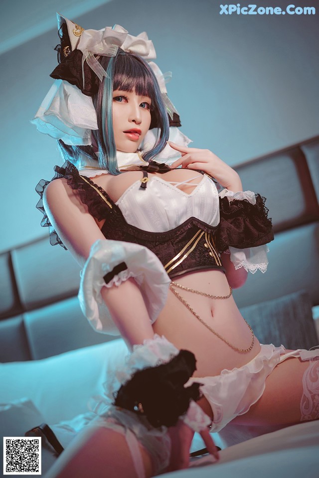 A woman in a maid outfit sitting on a bed.